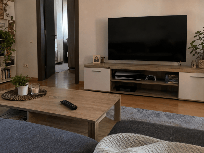 Televizor oprit pe un corp TV, într-un living de apartament, cu echipamente electronice dedesubt