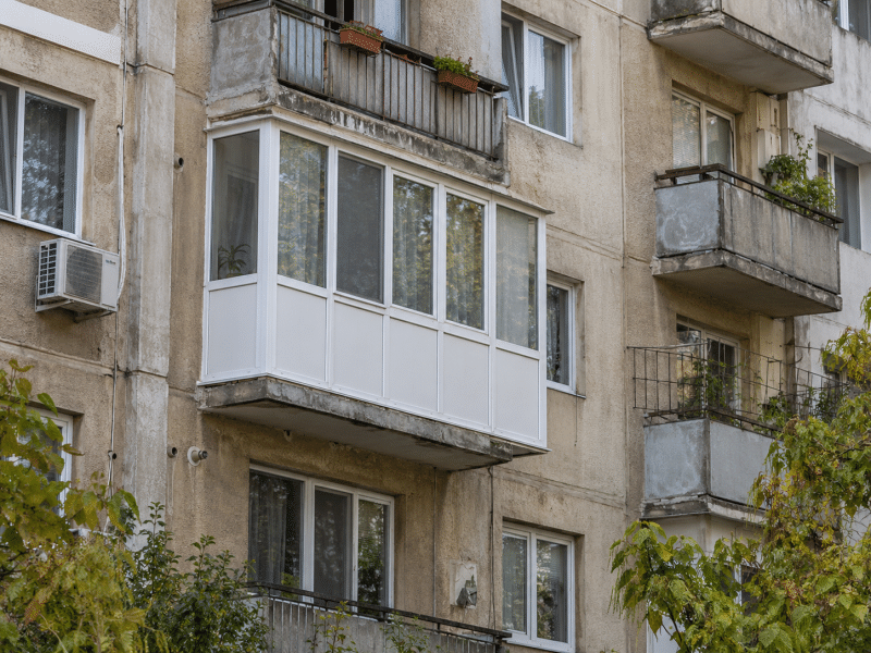 Balcon închis cu tâmplărie PVC albă, într-un bloc vechi din România, exemplu de modificare care poate necesita autorizație de construire.