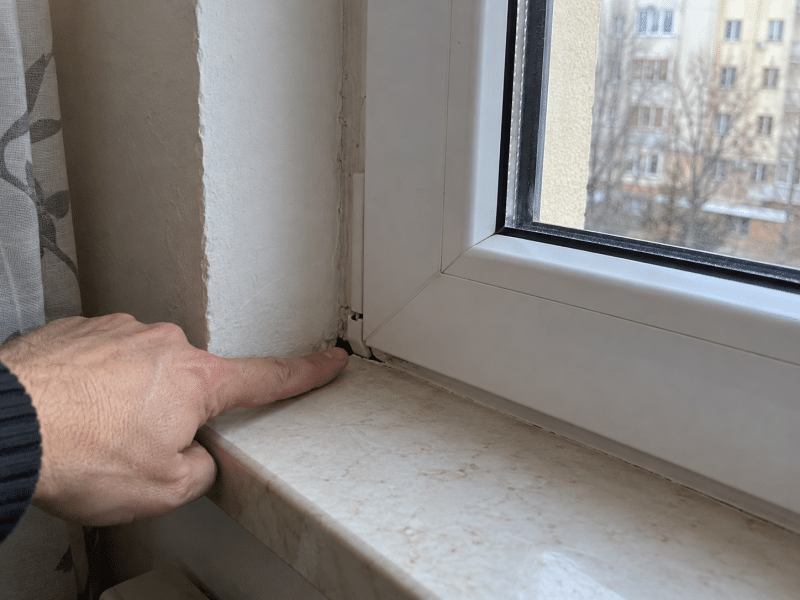 Persoană care indică un spațiu neetanș la îmbinarea dintre tocul ferestrei PVC, perete și glaful interior.